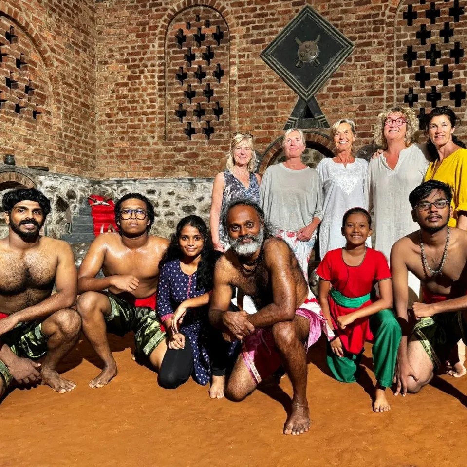 International students and local practitioners training together at Buddha Kalari Academy in traditional brick training hall with weapons display